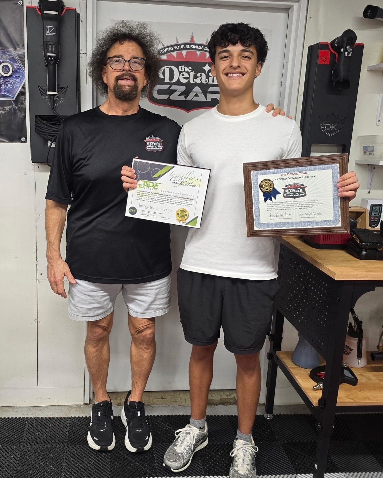 Shane holding his Jade Ceramic Coatings installer certificate and his Detail Czar Certified Detailer Licensee certificate, standing with his trainer at The Detail Czar